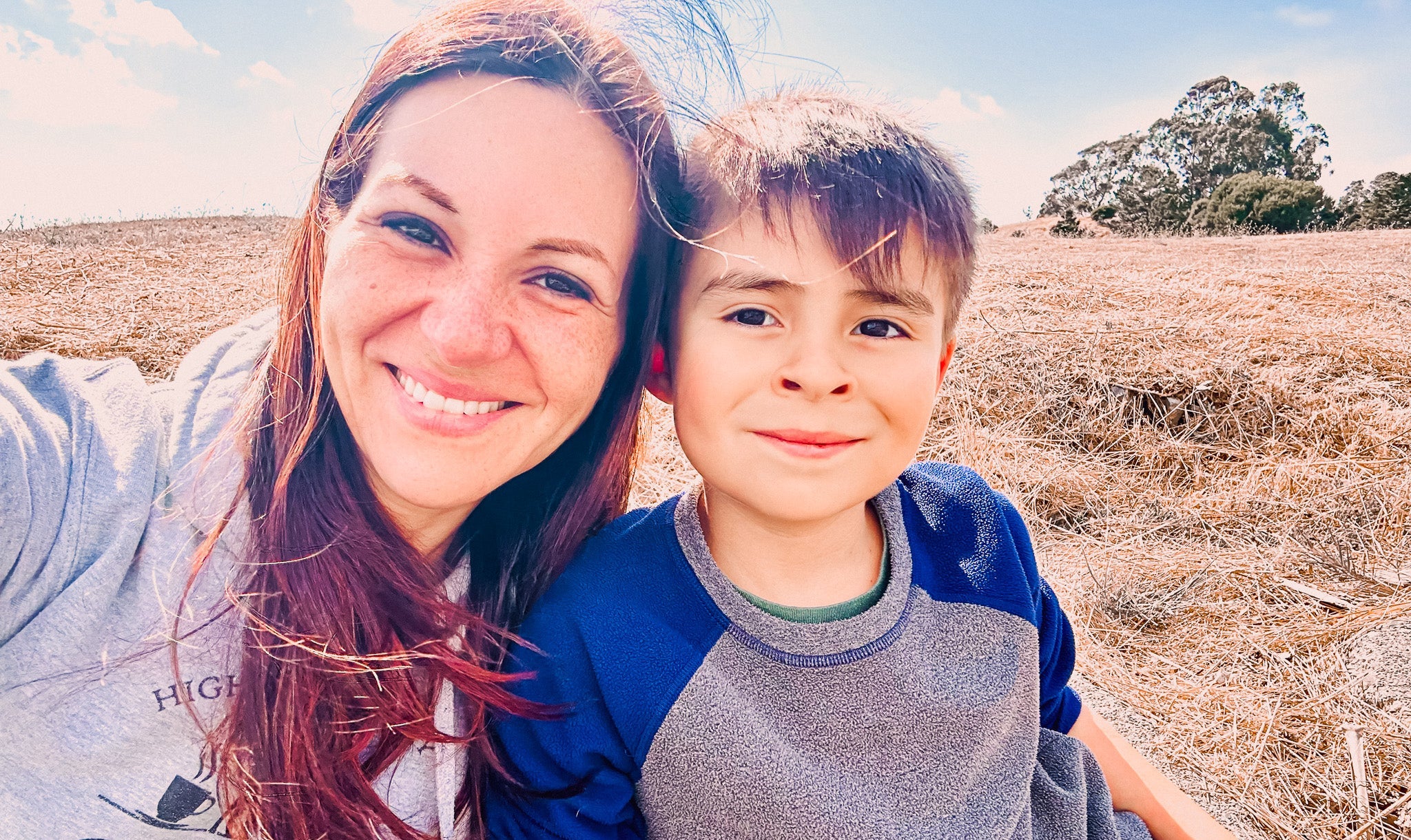 Woman and child sitting together in a field with trees in the background