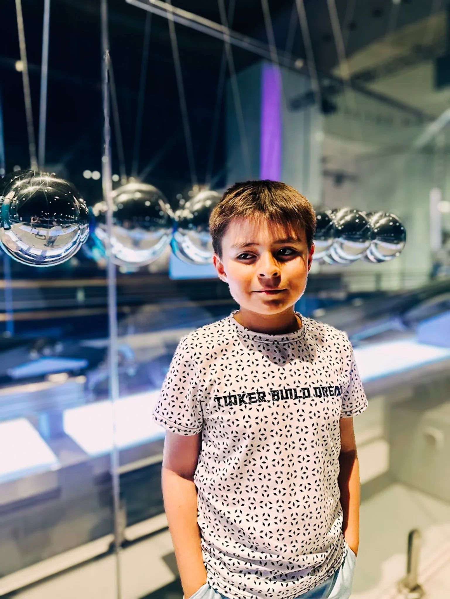 Child wearing a patterned shirt with text in front of reflective surfaces