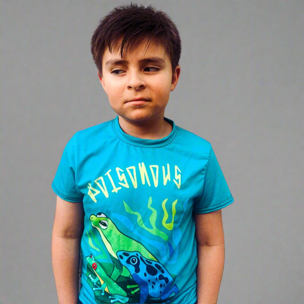 Child wearing a blue t-shirt with a frog graphic against a gray wall
