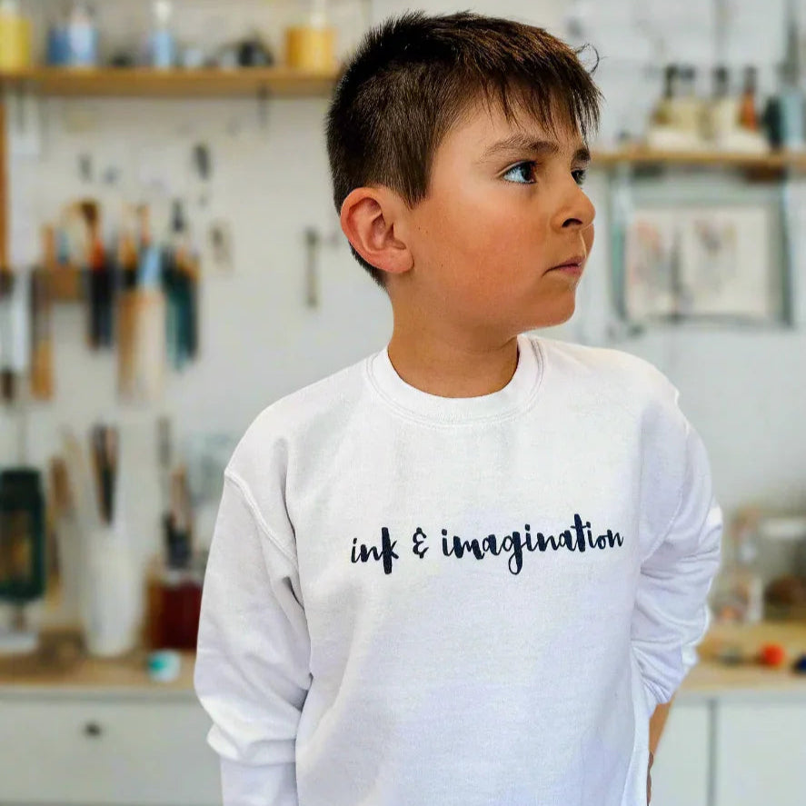 Child wearing a white sweatshirt with 'ink & imagination' text in a kitchen setting