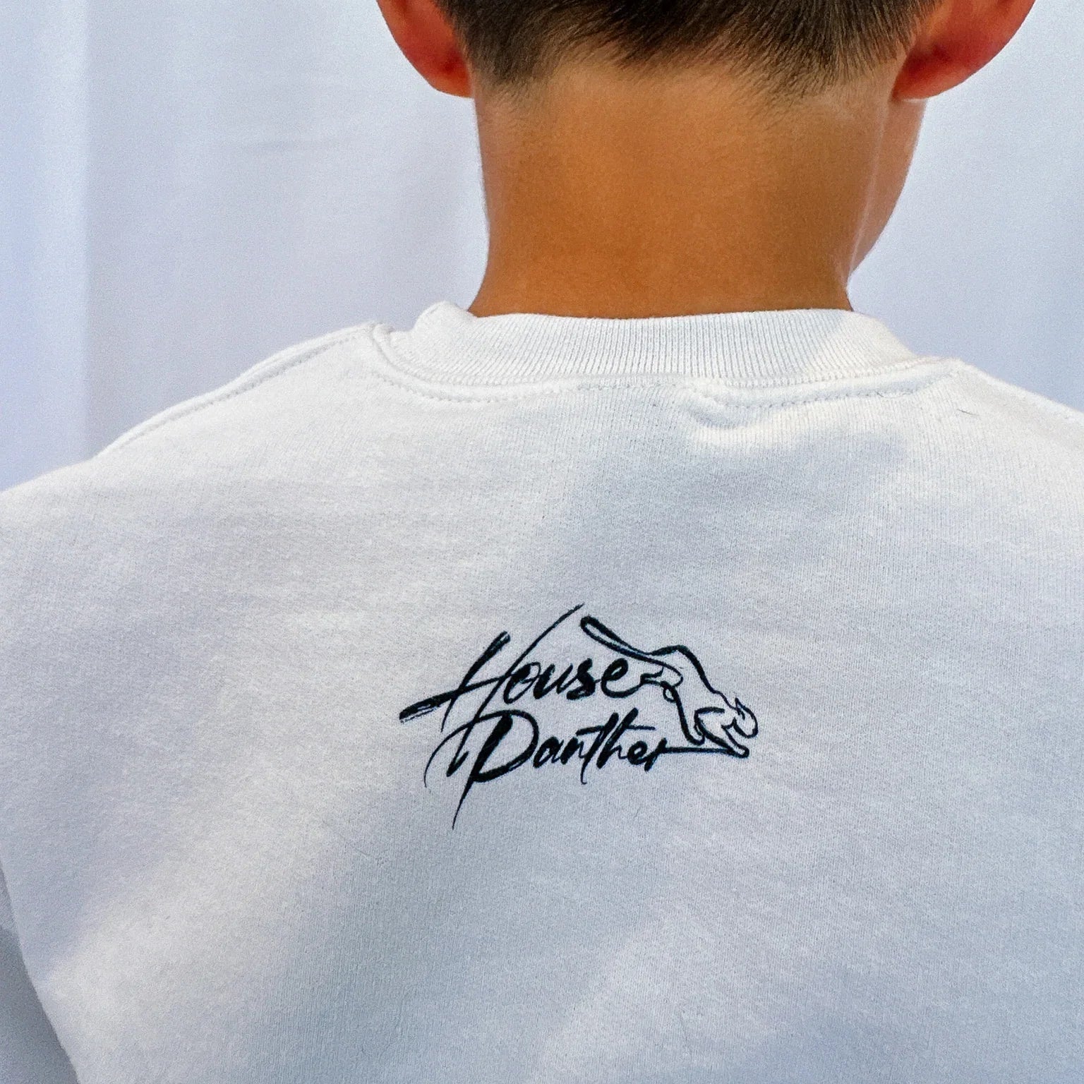 Person wearing a white t-shirt with a black logo on the back against a light background