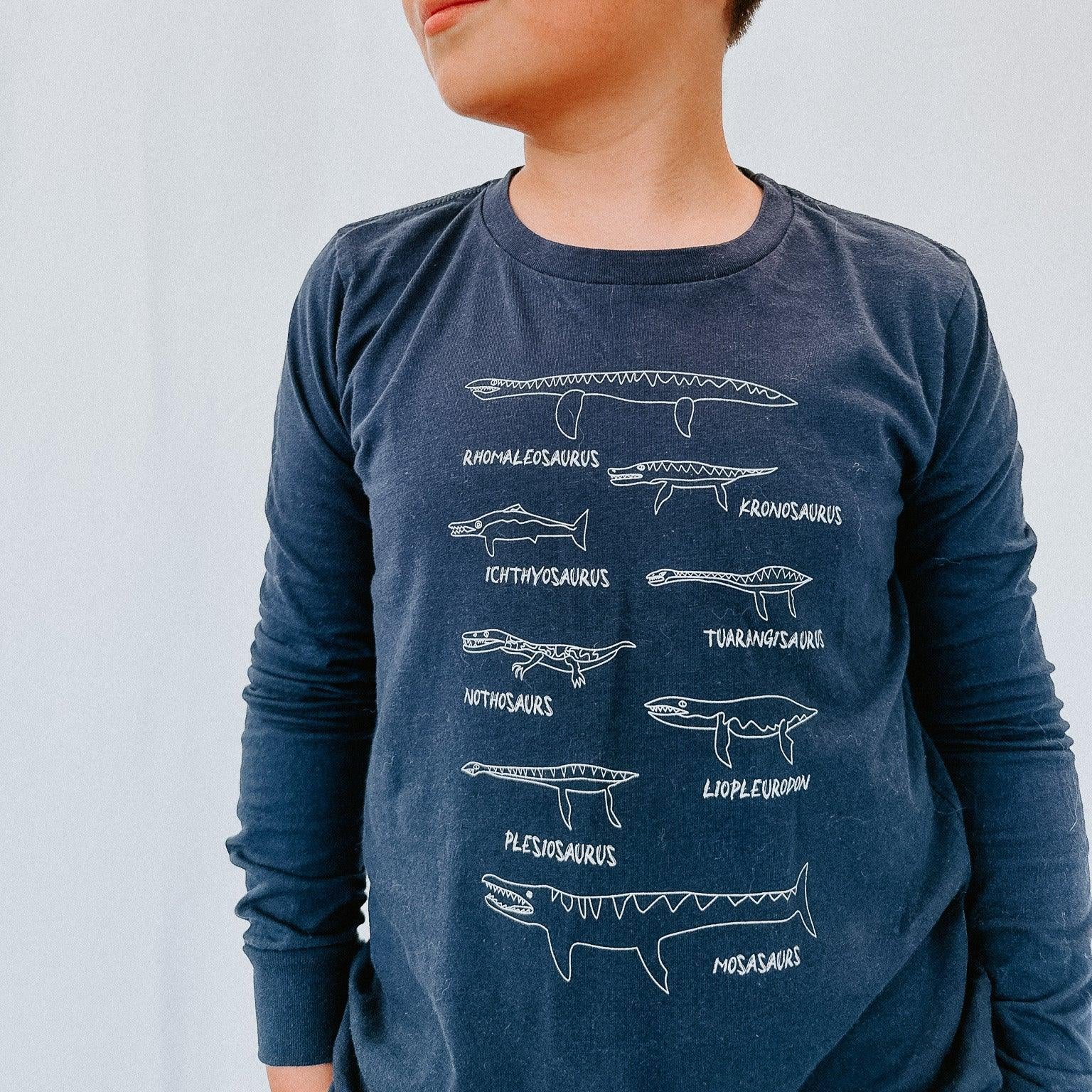 Child wearing a blue long-sleeve shirt with white dinosaur illustrations on a plain background